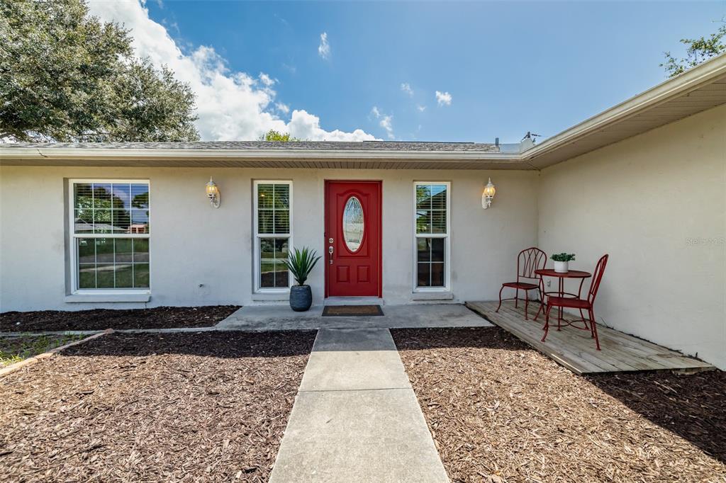 A single-story house exterior features a red front door, two windows, and a small porch — 6711 CONETTA DRIVE, SARASOTA, FL