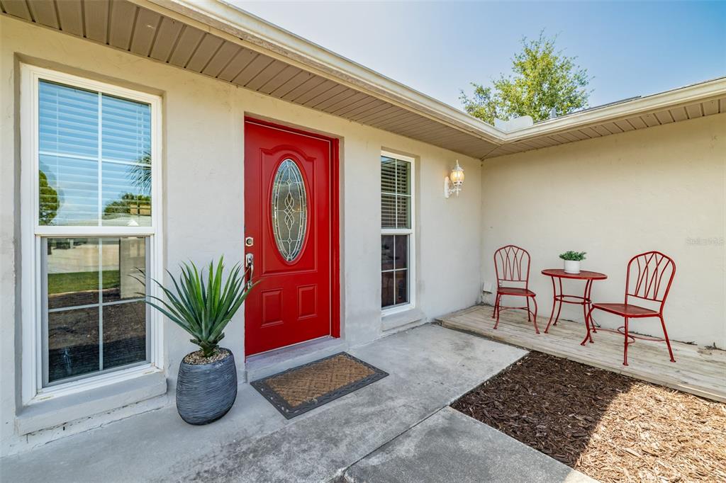 A bright red front door sits beside a small wooden patio with red metal furniture — 6711 CONETTA DRIVE, SARASOTA, FL