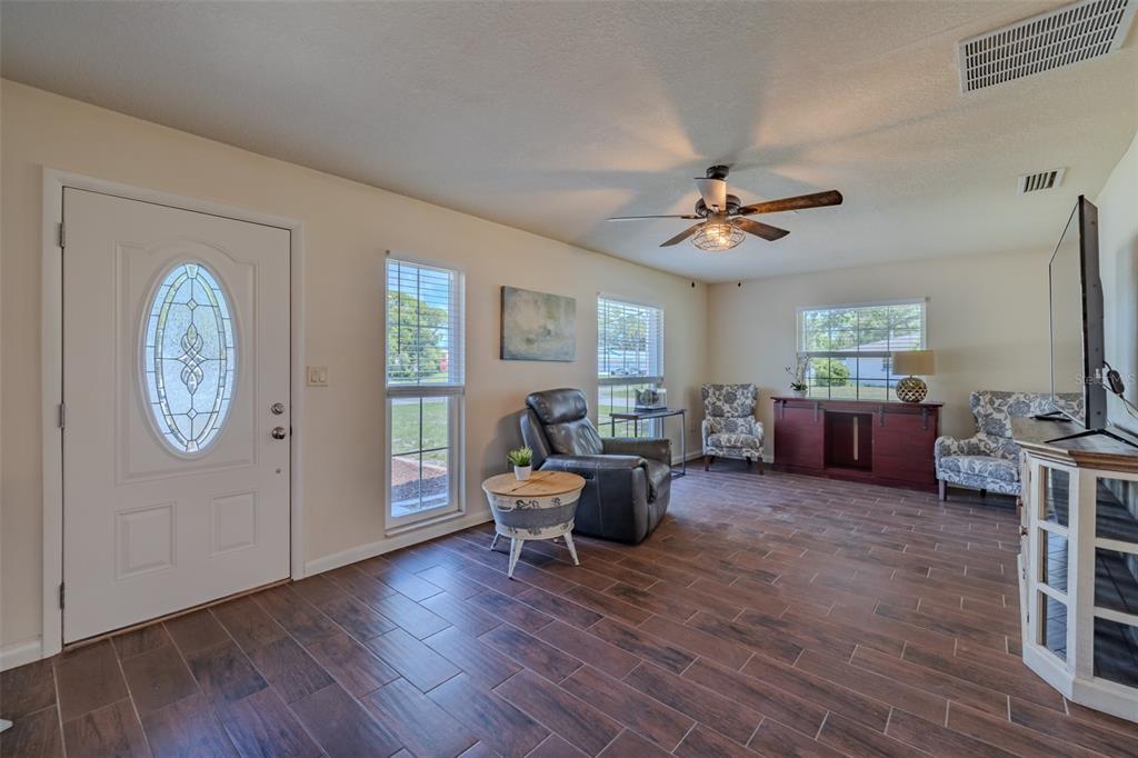A living room with wood-look tile flooring, a ceiling fan, and a front entry door — 6711 CONETTA DRIVE, SARASOTA, FL
