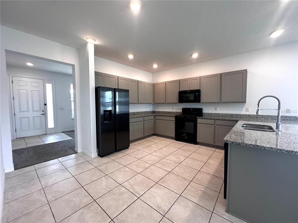 A kitchen features gray cabinets, granite countertops, black appliances, and light-colored tile flooring — 7580 SW 63RD LANE ROAD, OCALA, FL
