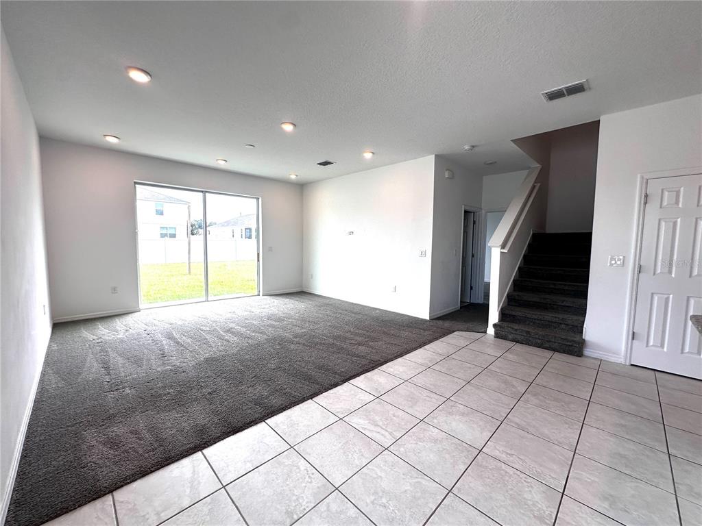 An open living area features gray carpeting, tile flooring, a sliding glass door, and stairs — 7580 SW 63RD LANE ROAD, OCALA, FL