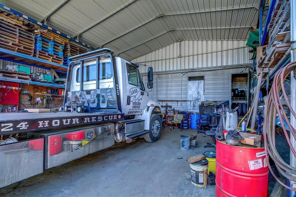 A large metal-sided workshop contains a white tow truck parked on a concrete floor — 29114 CORTEZ BOULEVARD, BROOKSVILLE, FL
