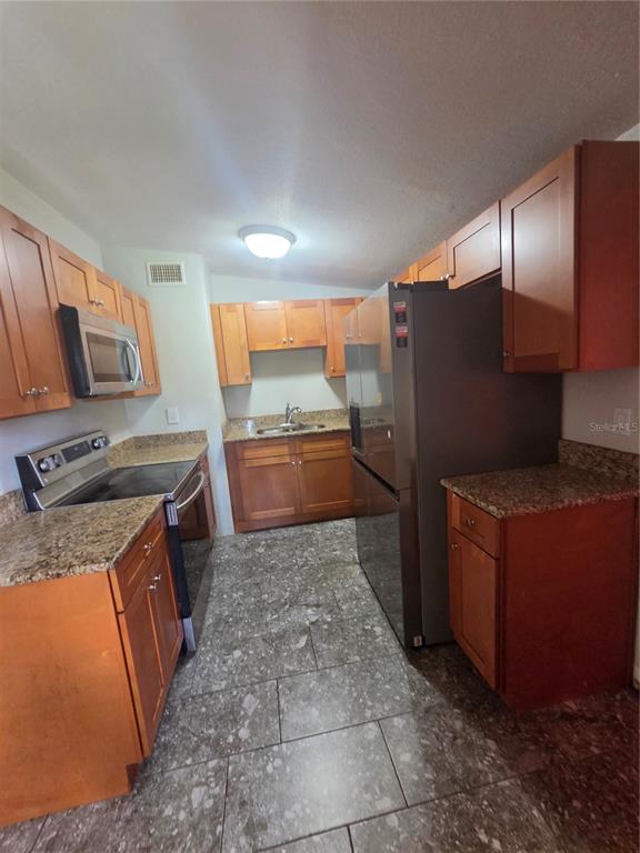 A galley kitchen features wood cabinets, granite countertops, stainless steel appliances, and gray tile flooring — 916 E 123RD AVENUE, TAMPA, FL