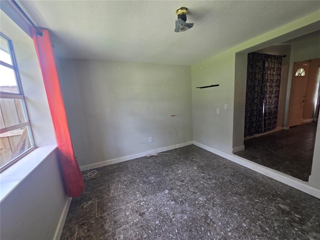 An empty room features gray tile flooring, a window with red curtains, and a ceiling light — 916 E 123RD AVENUE, TAMPA, FL