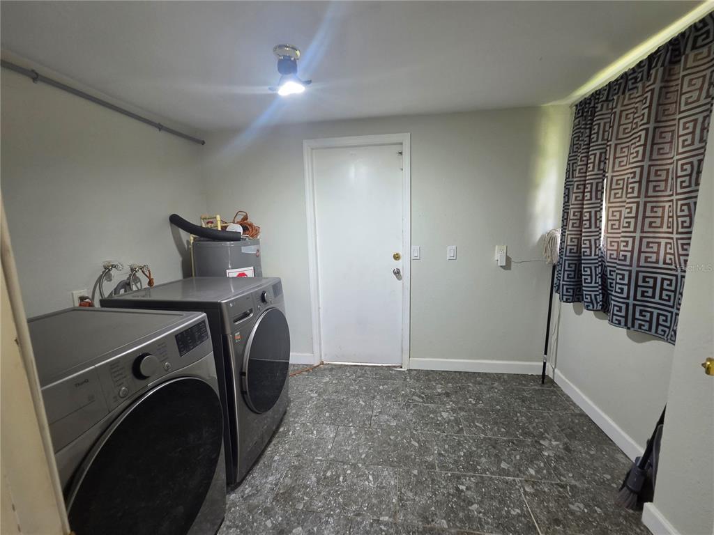 A laundry room features grey tile flooring, two front-loading appliances, and a white exterior door — 916 E 123RD AVENUE, TAMPA, FL