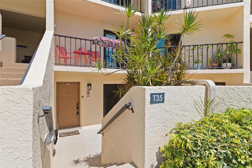 An exterior view of a tan building entrance with a balcony, stairs, and unit T35 — 7540 SUNSHINE SKYWAY LANE S UNIT T35, ST PETERSBURG, FL