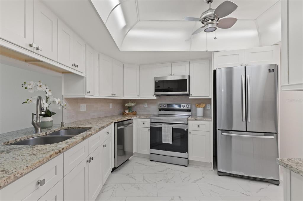 A kitchen with white cabinets, stainless steel appliances, granite countertops, and a tray ceiling — 7540 SUNSHINE SKYWAY LANE S UNIT T35, ST PETERSBURG, FL
