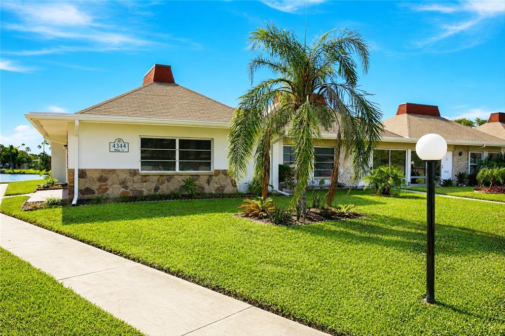 A single-story building with a stone facade, a palm tree, and a sidewalk on grass — 4344 TAHITIAN GARDENS CIRCLE UNIT D, HOLIDAY, FL