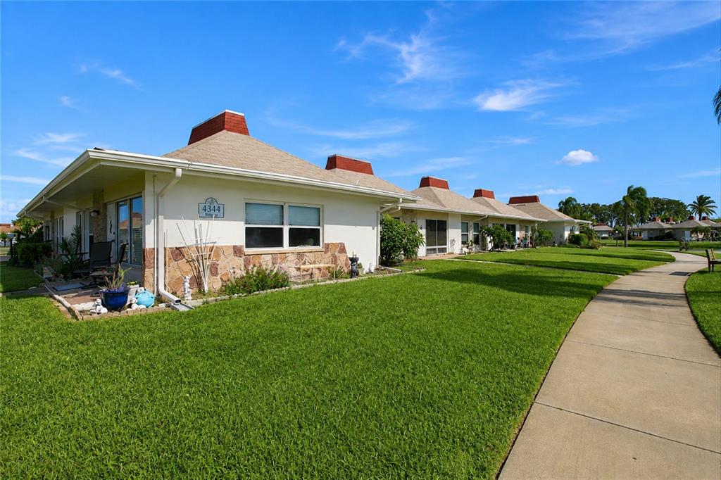 A row of single-story residential units with stone accents and brown roofs along a sidewalk — 4344 TAHITIAN GARDENS CIRCLE UNIT D, HOLIDAY, FL