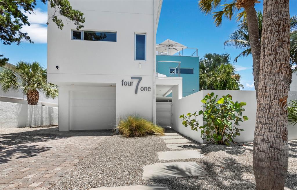 A modern white house with a garage and a turquoise accent wall under a blue sky — 471 ISLAND CIRCLE, SARASOTA, FL