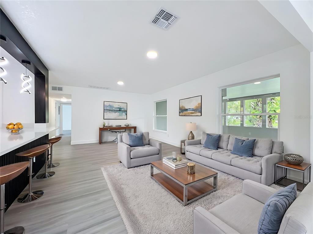 A modern living room features light wood floors, gray furniture, and a kitchen bar area — 3202 TRADEWINDS TRAIL, ORLANDO, FL