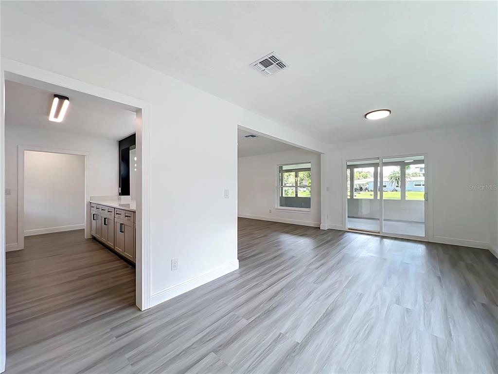 An open-concept living area with light wood-look flooring leads into a kitchen and sunroom — 3202 TRADEWINDS TRAIL, ORLANDO, FL