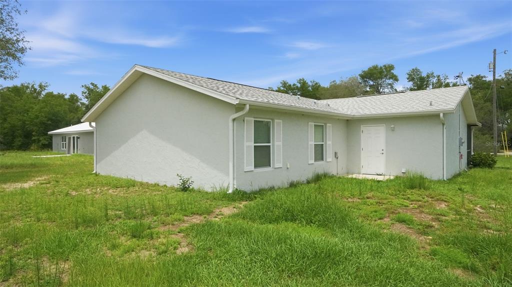 The exterior of a light-colored, single-story house with a white door and grassy yard — 30 MAPLE COURSE, OCKLAWAHA, FL