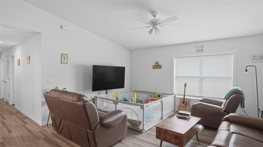 A living room features brown leather recliners, a television, and a playpen on wood flooring — 30 MAPLE COURSE, OCKLAWAHA, FL
