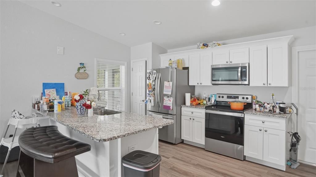 A kitchen features white cabinets, stainless steel appliances, granite countertops, and a breakfast bar island — 30 MAPLE COURSE, OCKLAWAHA, FL