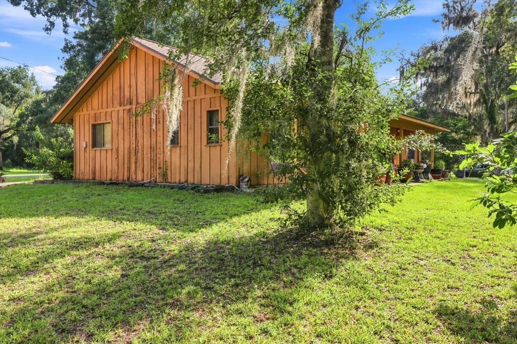 A wooden house with vertical siding sits on a grassy lawn under large trees — 4553 E SHOREWOOD DRIVE, HERNANDO, FL