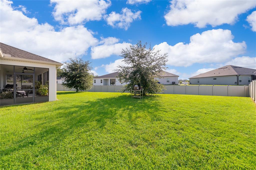 A grassy backyard features a screened-in patio, two trees, and a tall vinyl privacy fence — 1787 CHATSWORTH CIRCLE, ST CLOUD, FL