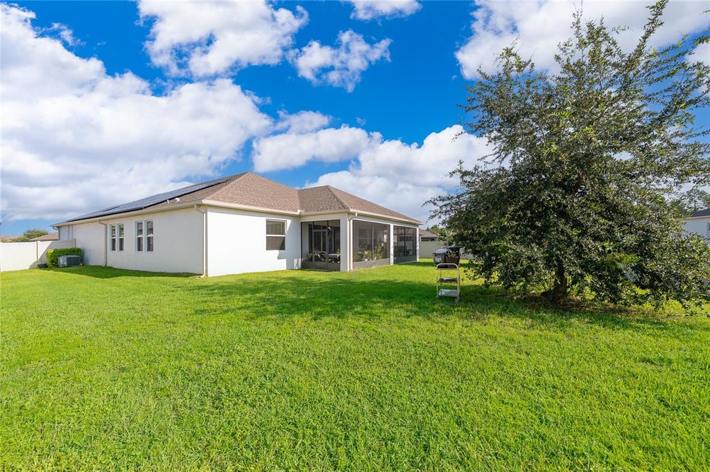 A backyard view of a single-story house with a screened-in patio and a large tree — 1787 CHATSWORTH CIRCLE, ST CLOUD, FL