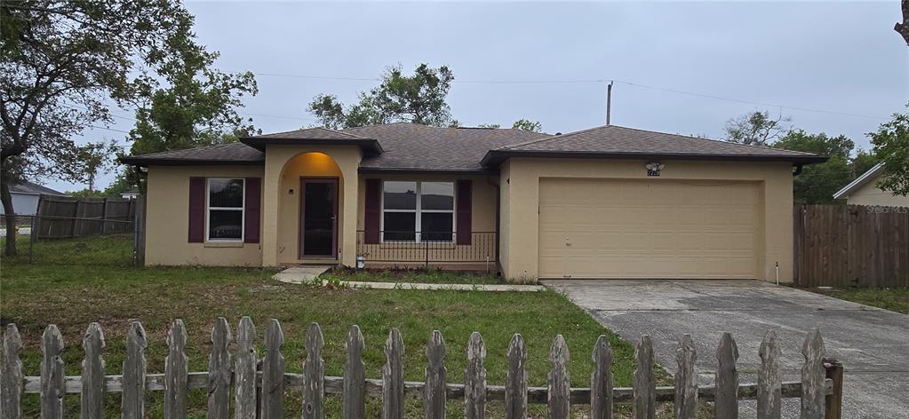 A single-story house with a beige stucco exterior, a two-car garage, and a wooden fence — 2729 SWEET SPRINGS STREET, DELTONA, FL