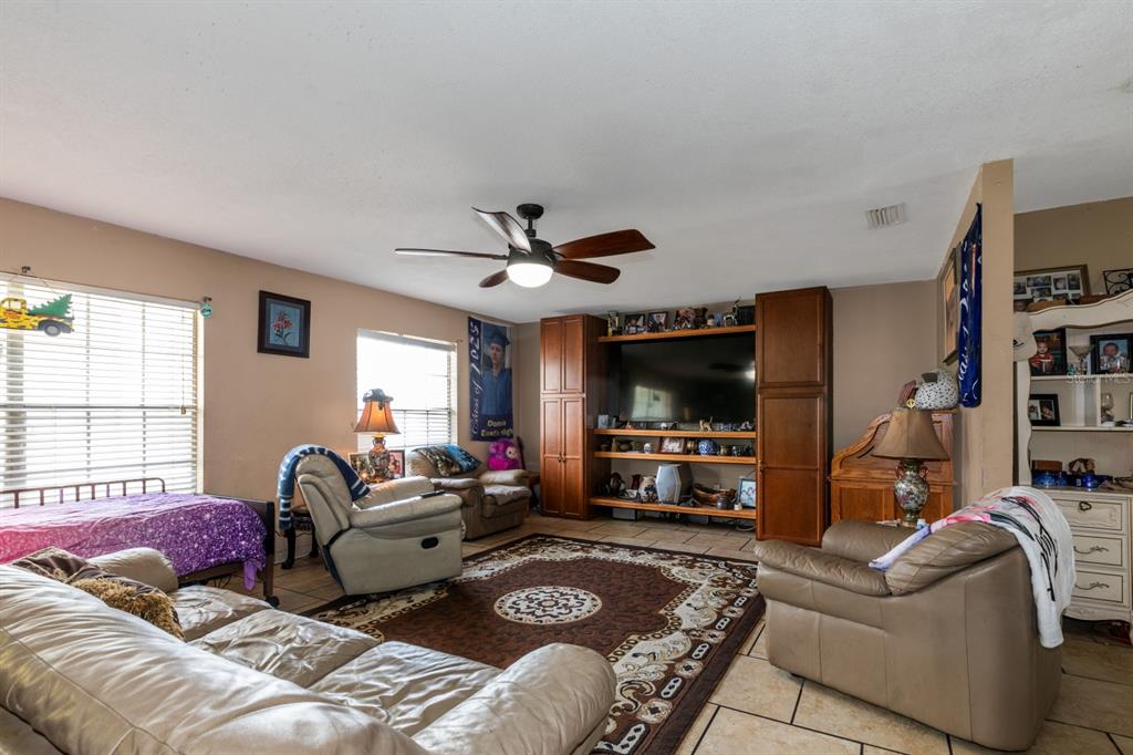 A living room features tile flooring, a ceiling fan, a large entertainment center, and furniture — 20024 STATE ROAD 44, EUSTIS, FL