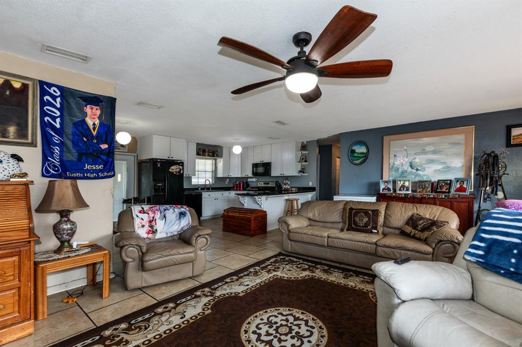 A living room with tile floors and a ceiling fan opens to a white kitchen — 20024 STATE ROAD 44, EUSTIS, FL