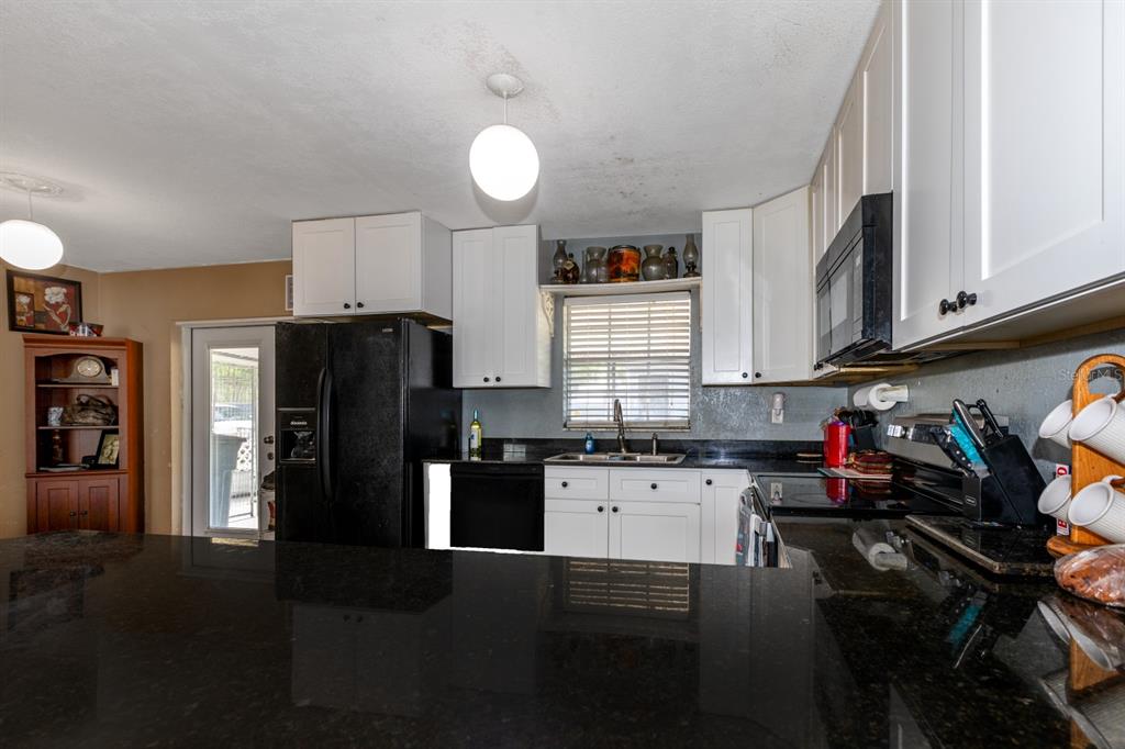 A kitchen features white cabinets, black appliances, dark granite countertops, and a central island — 20024 STATE ROAD 44, EUSTIS, FL