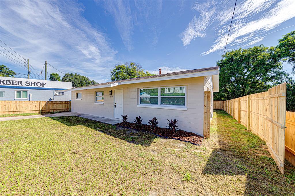 A single-story house with beige siding and a wooden fence stands under a blue sky — 703 S DIXIE AVENUE, FRUITLAND PARK, FL
