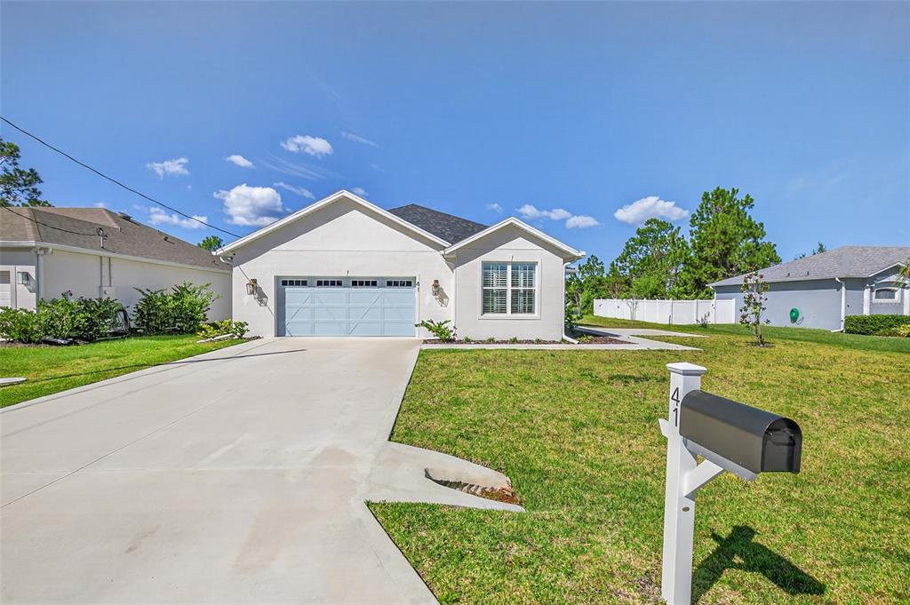 A single-story house with a light-colored exterior, a two-car garage, and a front lawn — 41 LA MANCHA DRIVE, PALM COAST, FL