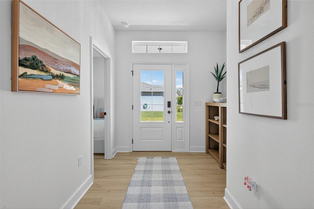A bright entryway features light wood flooring, a white front door, and framed wall art — 41 LA MANCHA DRIVE, PALM COAST, FL