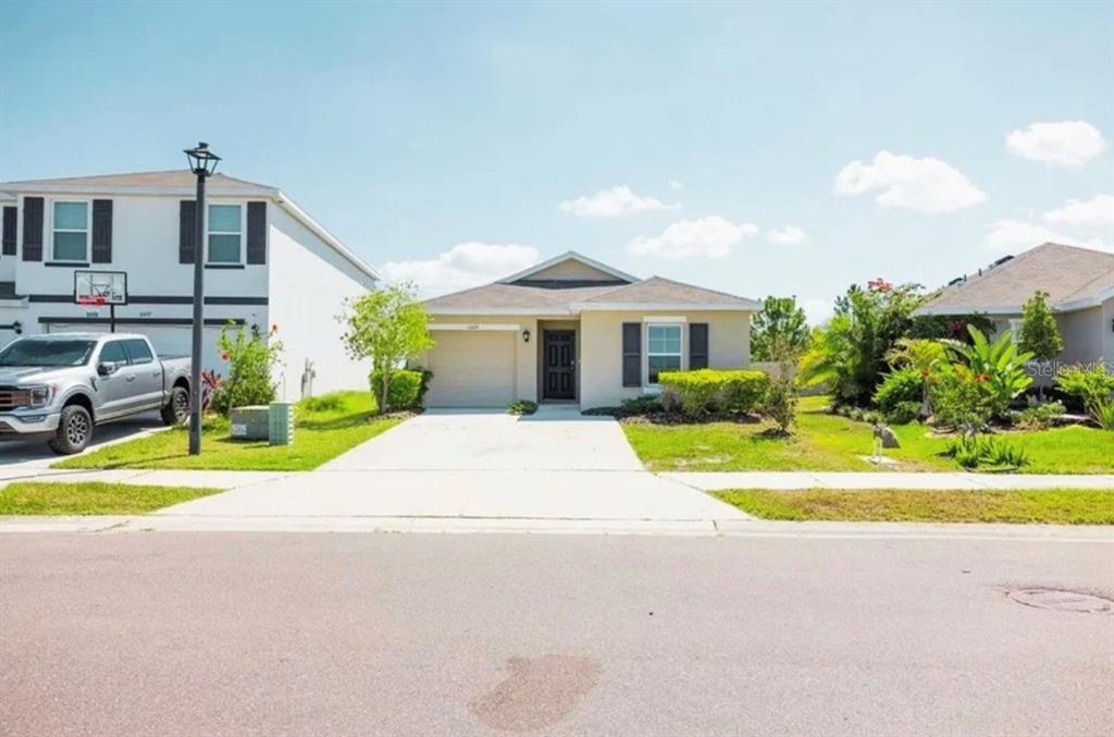 A single-story suburban house with a tan exterior, a garage, and a concrete driveway — 10428 FLATHEAD DRIVE, PARRISH, FL