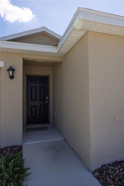 A tan stucco home exterior features a recessed entryway with a dark front door — 10428 FLATHEAD DRIVE, PARRISH, FL