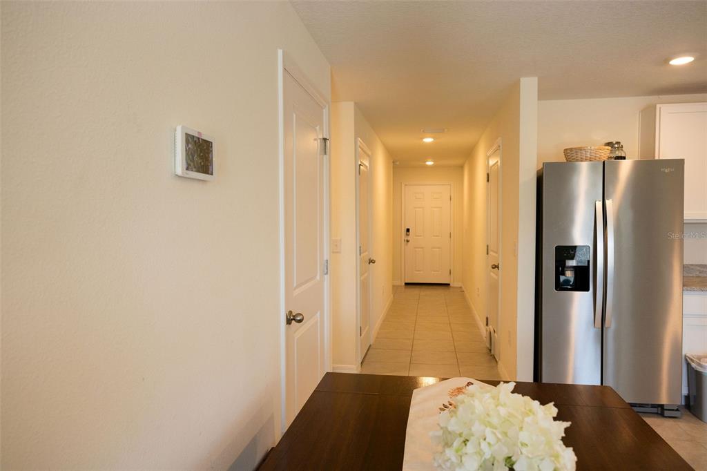 A hallway with tile flooring leads to a white front door near a stainless refrigerator — 10428 FLATHEAD DRIVE, PARRISH, FL