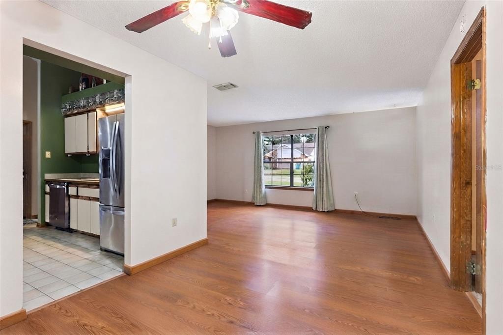 A living room with wood-look flooring and a ceiling fan opens into a kitchen area — 217 HARBOR DRIVE, WINTER GARDEN, FL