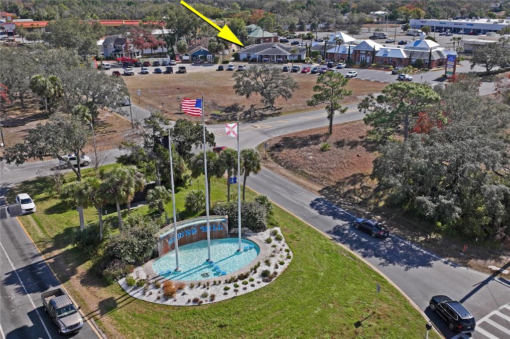 An aerial view shows a commercial building with a parking lot behind a fountain monument — 5300 SPRING HILL DRIVE, SPRING HILL, FL
