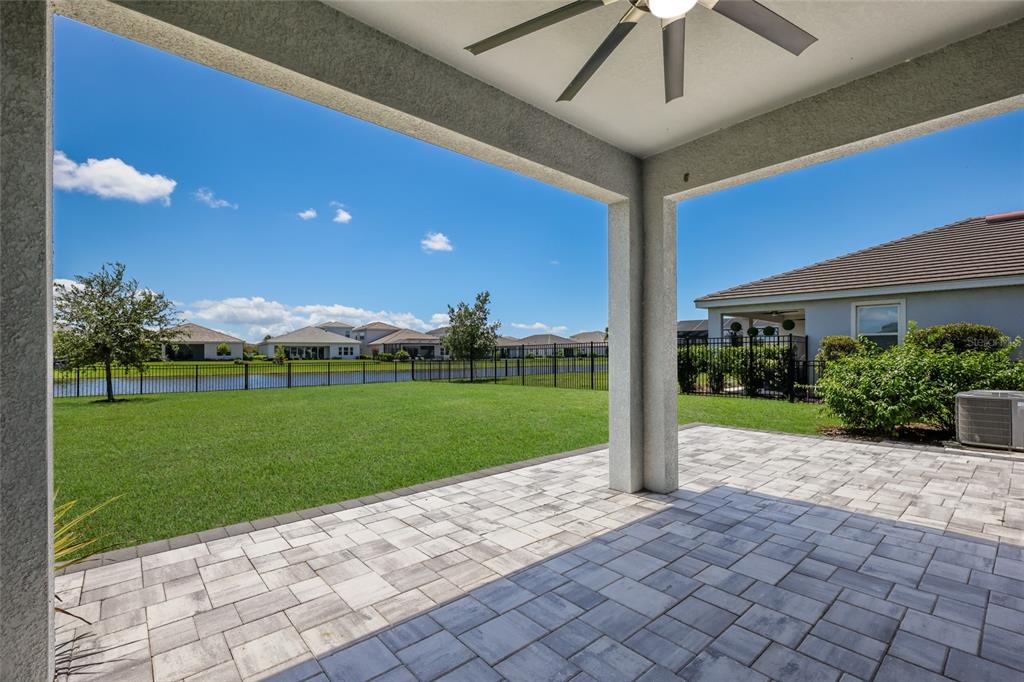 A covered patio with paver flooring overlooks a grassy backyard, a pond, and neighboring houses — 17828 GULF RANCH PLACE, LAKEWOOD RANCH, FL