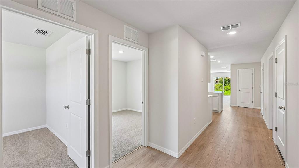 A hallway with wood-look flooring leads to a kitchen, with carpeted rooms on the left — 1142 BOURBON AVENUE, PARRISH, FL