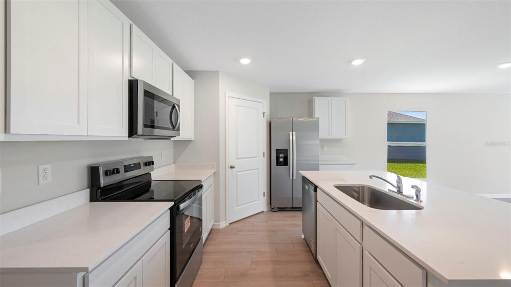 A modern kitchen features white cabinets, stainless steel appliances, and a central island with sink — 1142 BOURBON AVENUE, PARRISH, FL