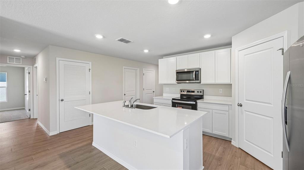 A modern kitchen features white cabinetry, a central island with a sink, and light flooring — 1142 BOURBON AVENUE, PARRISH, FL