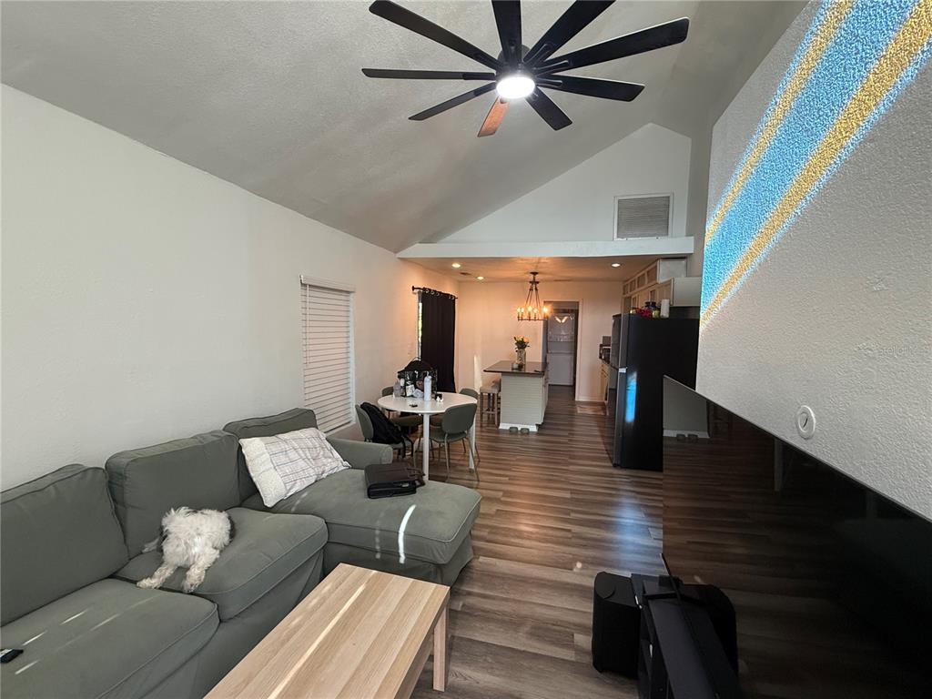 A living room with vaulted ceilings, gray sectional sofa, and an open kitchen area — 7309 N HUNTLEY AVENUE, TAMPA, FL
