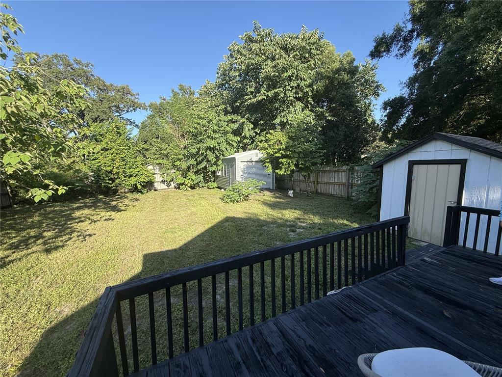 A wooden deck overlooks a grassy backyard with two storage sheds and mature trees — 7309 N HUNTLEY AVENUE, TAMPA, FL