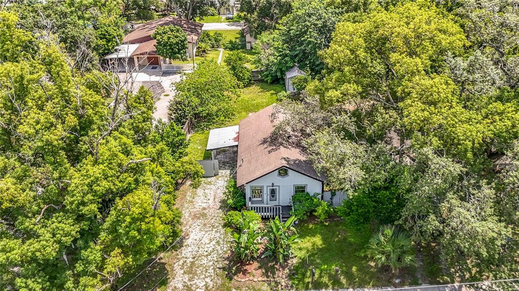 An aerial view shows a single-story house with a brown roof surrounded by dense trees — 7309 N HUNTLEY AVENUE, TAMPA, FL