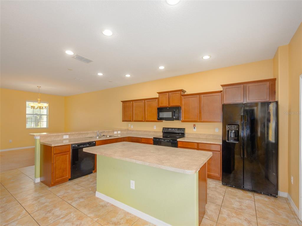 A kitchen features wood cabinets, black appliances, a central island, and light-colored tile flooring — 1300 SEBURN ROAD, APOPKA, FL