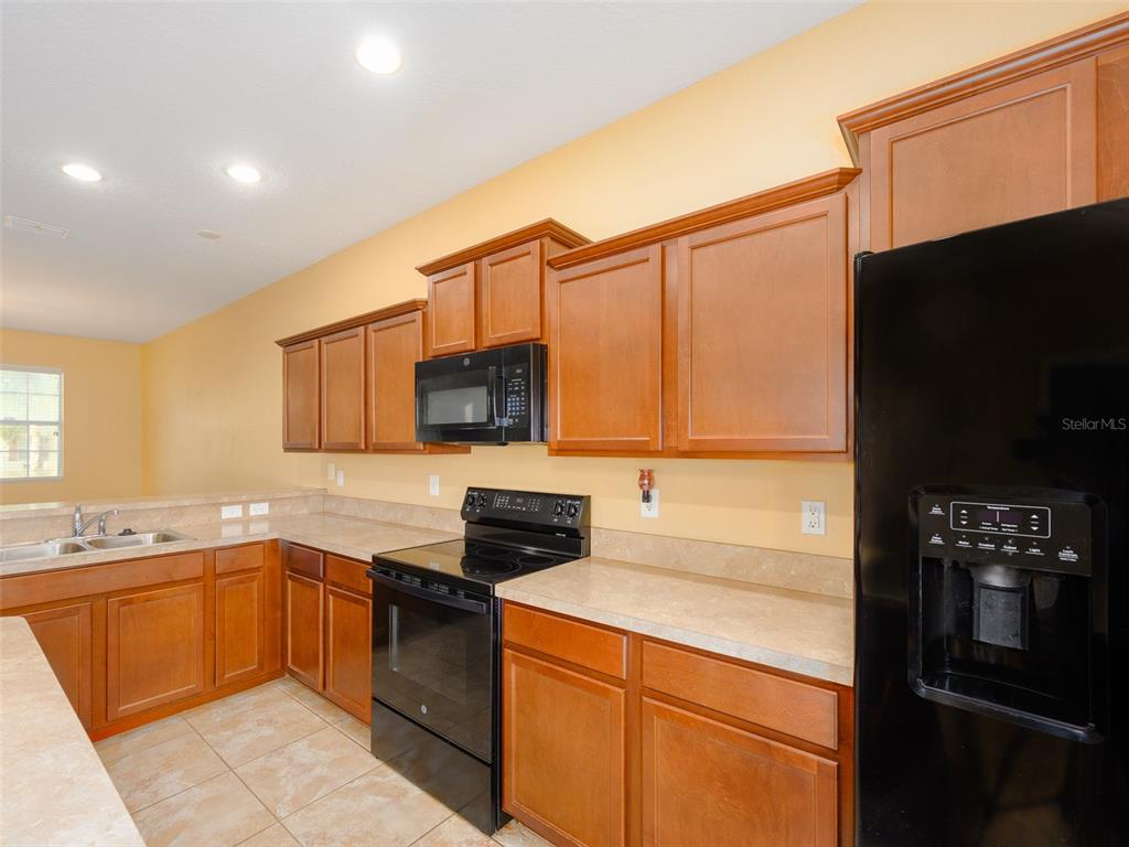 A kitchen features wooden cabinets, black appliances, and light-colored countertops against yellow walls — 1300 SEBURN ROAD, APOPKA, FL