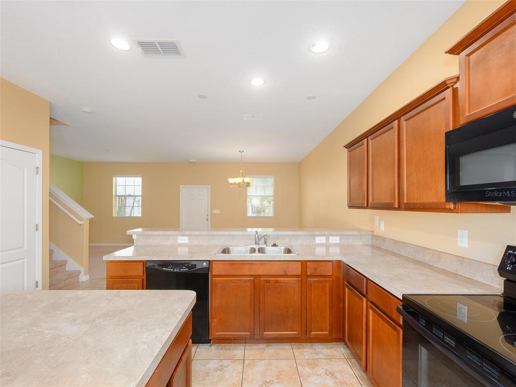 A kitchen with wood cabinets, laminate countertops, and black appliances overlooks an adjacent living area — 1300 SEBURN ROAD, APOPKA, FL