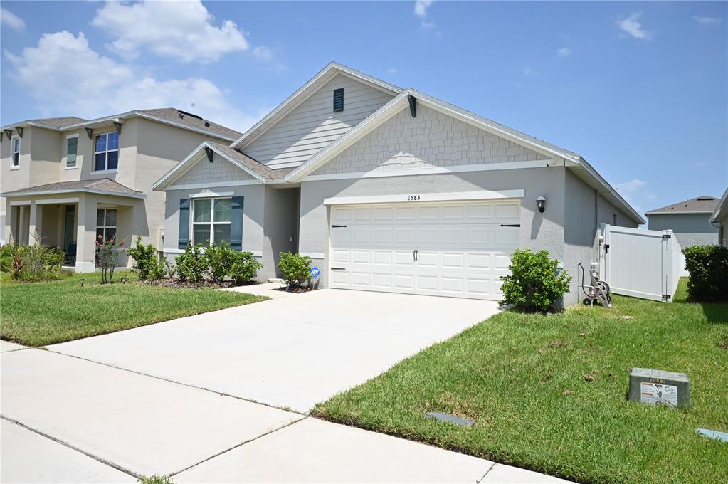 A single-story house with a gray stucco exterior, a two-car garage, and a front window — 1583 BARBERRY DRIVE, KISSIMMEE, FL