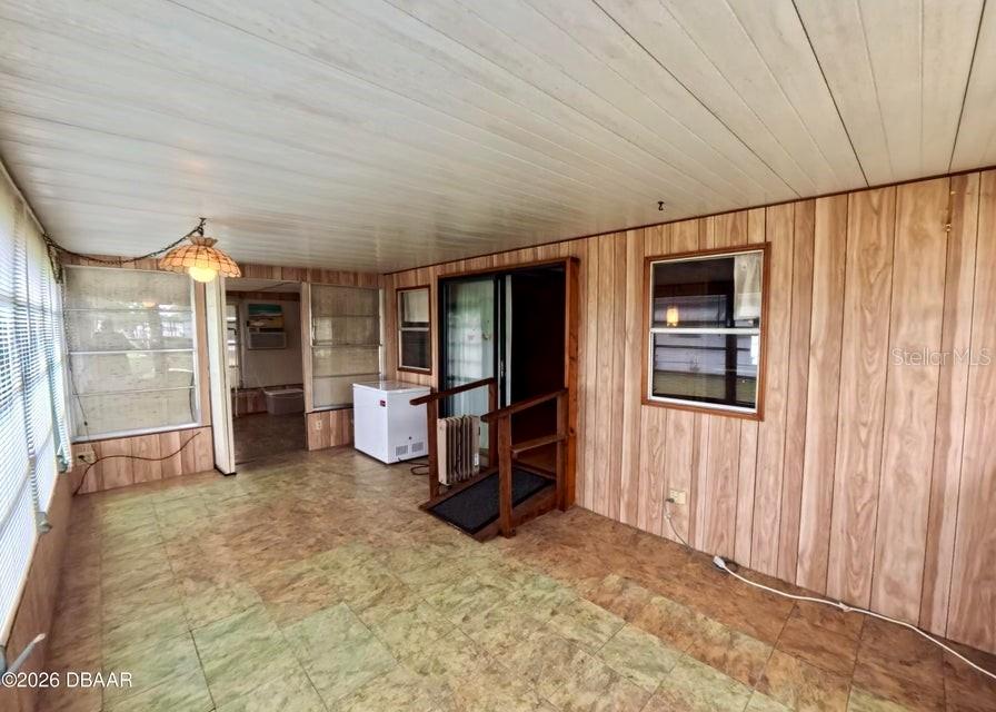 A sunroom features wood-paneled walls, tiled flooring, a sliding glass door, and a small ramp — 725 MARSHALL CIRCLE, PORT ORANGE, FL