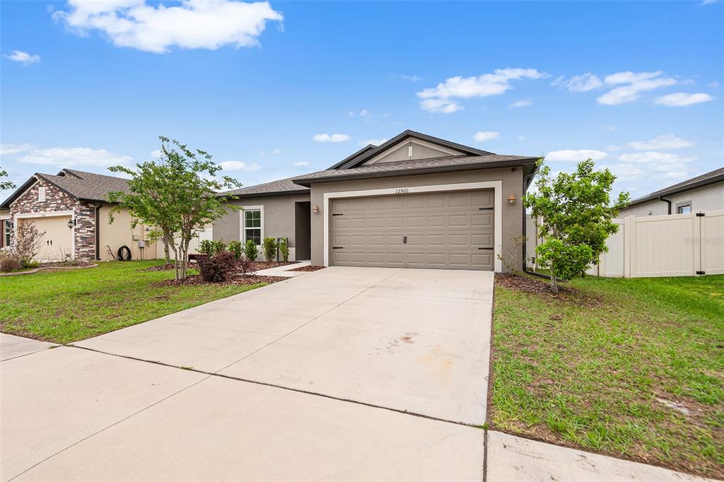 A single-story house with a beige exterior, a two-car garage, and a concrete driveway — 12960 CONQUISTADOR LOOP, SPRING HILL, FL