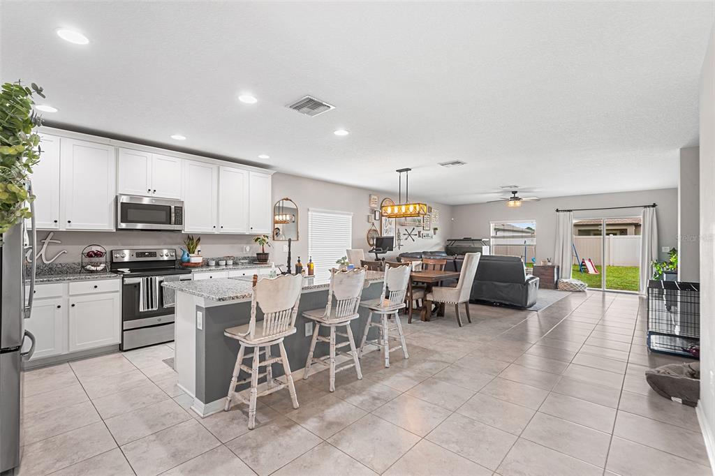 An open-concept kitchen and living area features white cabinets, granite countertops, and tile flooring — 12960 CONQUISTADOR LOOP, SPRING HILL, FL