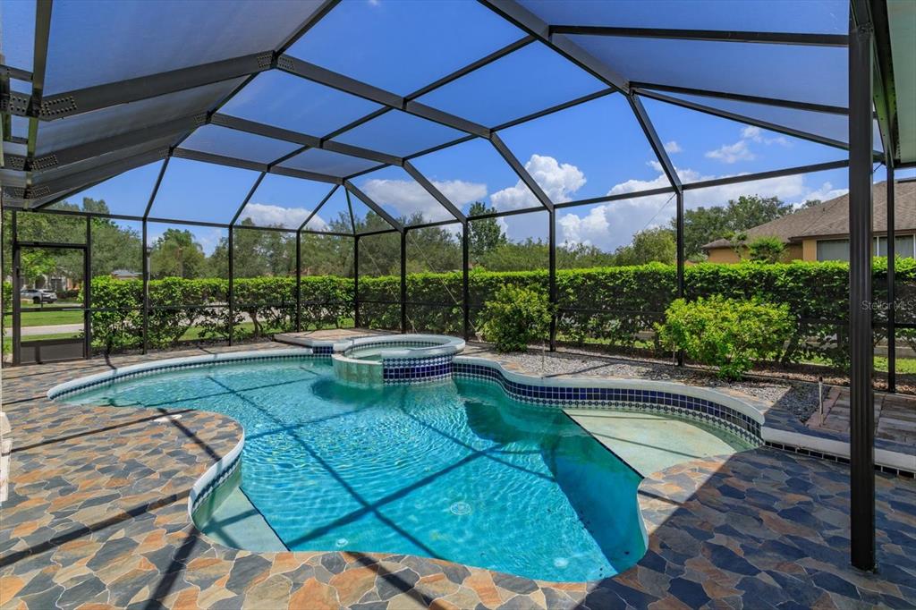 A screened-in swimming pool and hot tub with a stone-tiled deck and hedge landscaping — 606 BUCKHAVEN LOOP, OCOEE, FL
