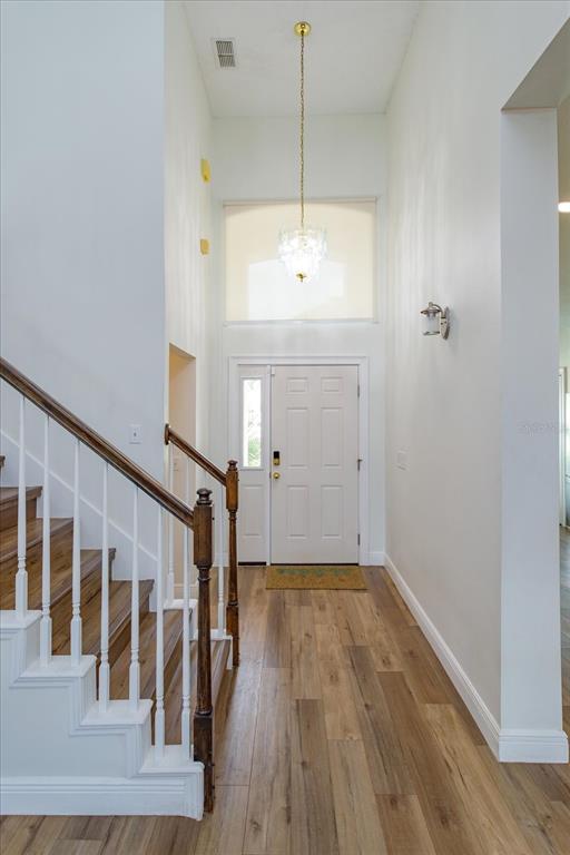 A bright entryway features wood-look flooring, a staircase with a wooden railing, and a chandelier — 606 BUCKHAVEN LOOP, OCOEE, FL